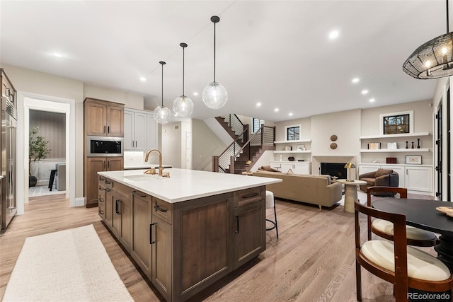 kitchen with built in microwave, an island with sink, sink, and pendant lighting