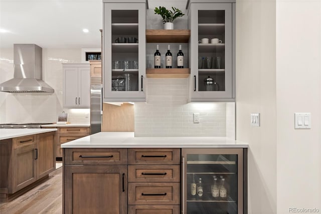 bar featuring wall chimney exhaust hood, backsplash, stainless steel built in refrigerator, and beverage cooler
