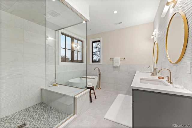 full bathroom featuring a freestanding bath, a tile shower, a sink, tile walls, and visible vents