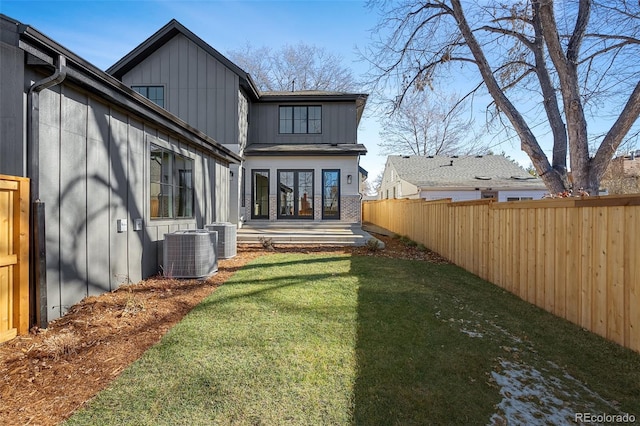 back of house with central AC unit, board and batten siding, a fenced backyard, and a yard