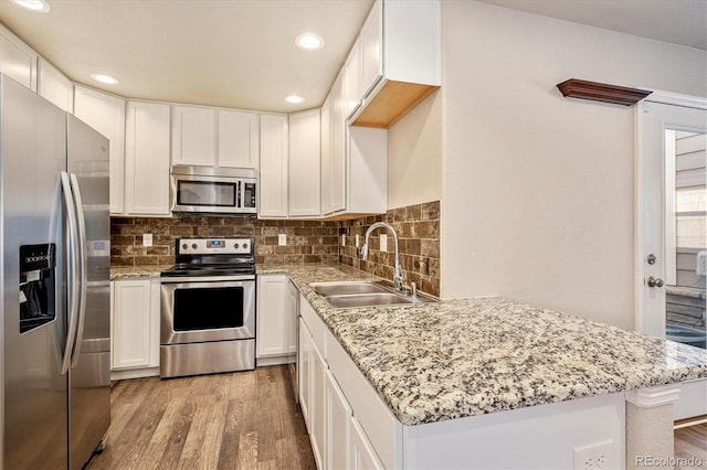 kitchen with a peninsula, a sink, appliances with stainless steel finishes, decorative backsplash, and light wood finished floors