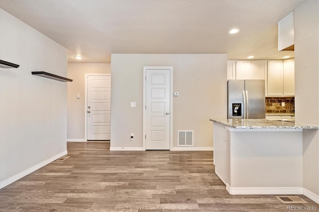 kitchen featuring wood finished floors, visible vents, white cabinets, stainless steel fridge with ice dispenser, and light stone countertops