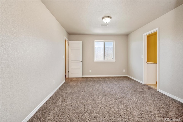 carpeted empty room featuring visible vents, baseboards, a textured ceiling, and a textured wall