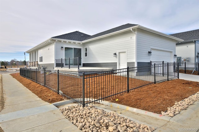 view of property exterior featuring concrete driveway, fence, a garage, and a shingled roof