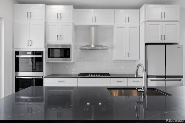 kitchen featuring stainless steel appliances, decorative backsplash, white cabinetry, dark countertops, and wall chimney exhaust hood