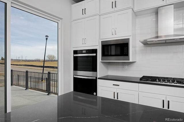 kitchen featuring dark countertops, tasteful backsplash, exhaust hood, white cabinets, and stainless steel appliances