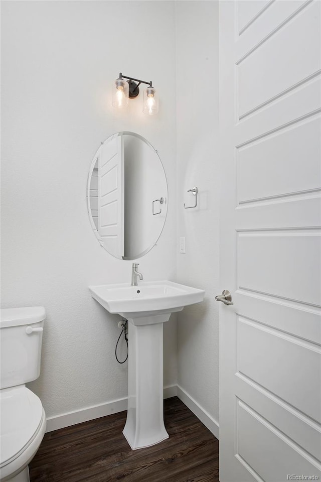 half bathroom featuring toilet, wood finished floors, and baseboards