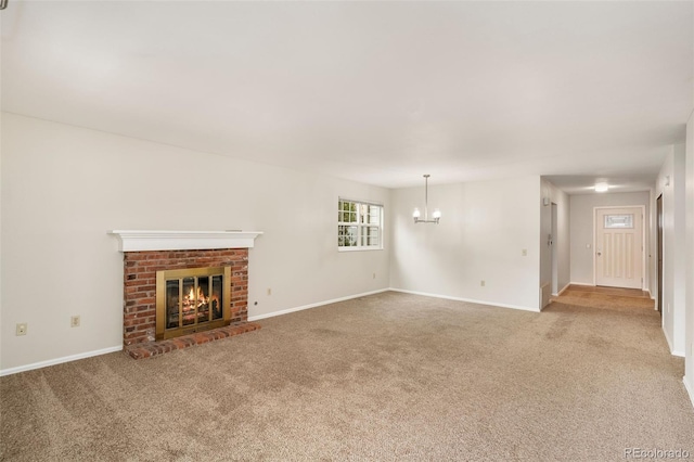 unfurnished living room featuring a chandelier, carpet flooring, a brick fireplace, and baseboards