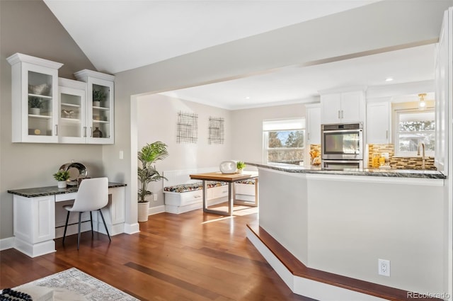 kitchen with dark stone countertops, white cabinets, double oven, and kitchen peninsula