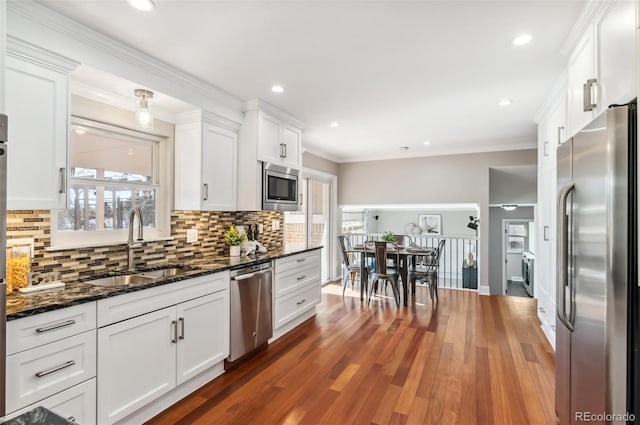 kitchen with sink, appliances with stainless steel finishes, white cabinetry, dark stone countertops, and dark hardwood / wood-style flooring