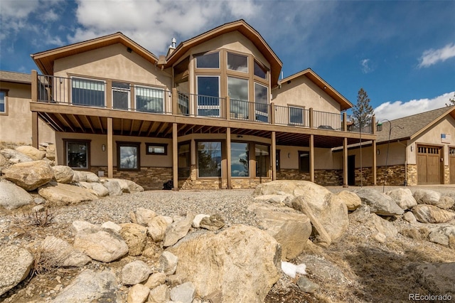 rear view of house with a garage, stone siding, and stucco siding