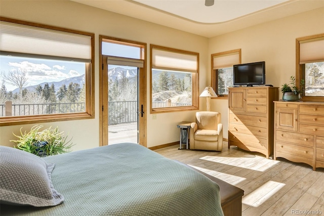 bedroom featuring access to outside, a mountain view, light wood-style flooring, and baseboards