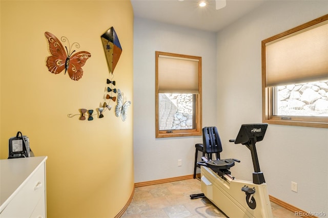 exercise room with a ceiling fan and baseboards