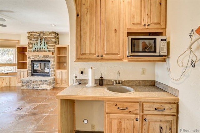 kitchen featuring stainless steel microwave, a fireplace, a sink, and tile counters