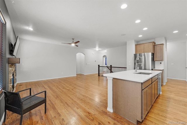 kitchen featuring ceiling fan, light hardwood / wood-style flooring, stainless steel refrigerator with ice dispenser, and an island with sink