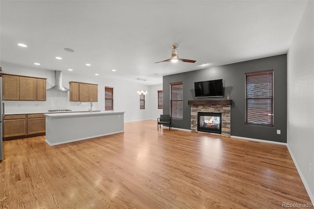 kitchen featuring light hardwood / wood-style floors, a stone fireplace, a kitchen island with sink, and wall chimney exhaust hood