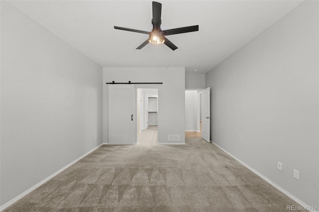 unfurnished bedroom with ceiling fan, a barn door, a walk in closet, and light carpet