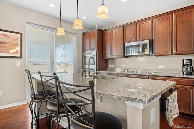 kitchen featuring an island with sink, appliances with stainless steel finishes, dark wood-style flooring, and hanging light fixtures