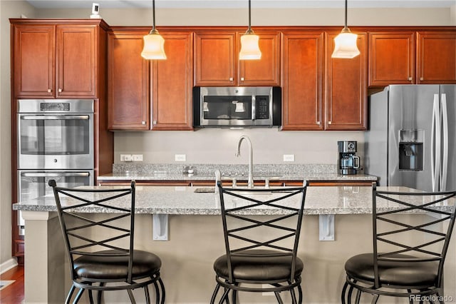 kitchen with stainless steel appliances, a breakfast bar, an island with sink, and decorative light fixtures