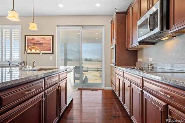 kitchen with light stone counters, appliances with stainless steel finishes, dark wood-style flooring, pendant lighting, and a sink