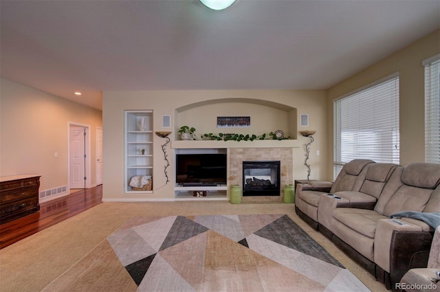 living room featuring light carpet, built in shelves, and a tile fireplace