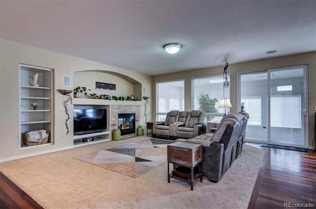 living room with a tiled fireplace, built in shelves, and wood-type flooring