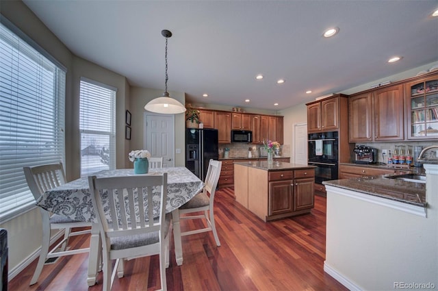 kitchen featuring decorative light fixtures, sink, dark stone countertops, a center island, and black appliances