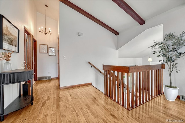 hall with an upstairs landing, high vaulted ceiling, wood finished floors, beamed ceiling, and a chandelier