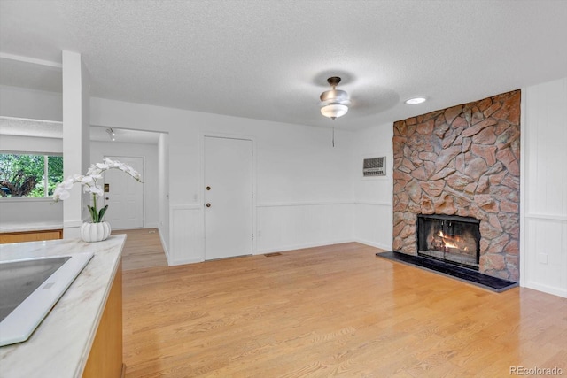 8705 W 86th Dr, Arvada, CO 80005 - unfurnished living room with a textured ceiling, ceiling fan, a stone fireplace, and light wood finished floors