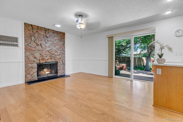 8705 W 86th Dr, Arvada, CO 80005 - unfurnished living room featuring a textured ceiling, wood finished floors, a wall mounted AC, a ceiling fan, and a fireplace