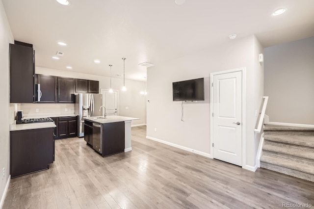 kitchen featuring an island with sink, decorative light fixtures, stainless steel appliances, light countertops, and light wood-style floors