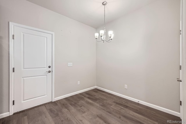 empty room featuring a notable chandelier, dark wood-type flooring, and baseboards