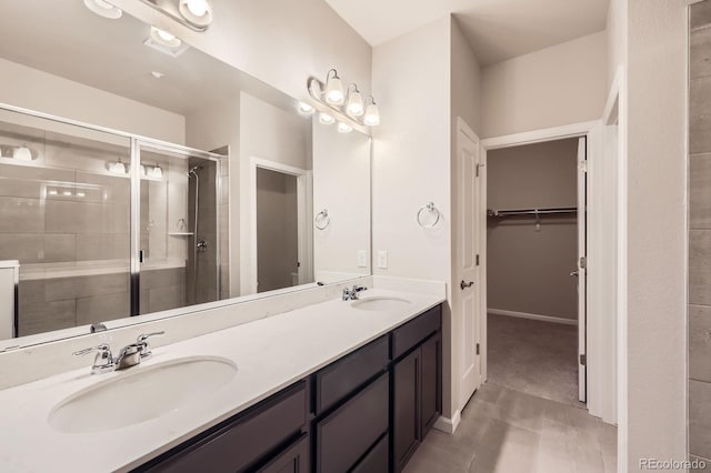 full bath featuring double vanity, a spacious closet, a stall shower, and a sink