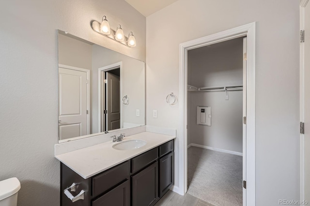 bathroom featuring baseboards, vanity, toilet, and a spacious closet