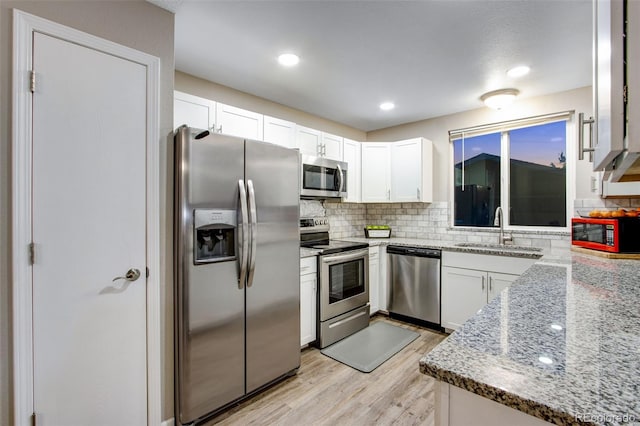 kitchen with sink, light wood-type flooring, white cabinetry, appliances with stainless steel finishes, and light stone counters