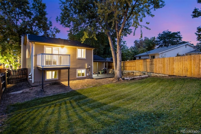 back house at dusk featuring a patio, a lawn, and a balcony