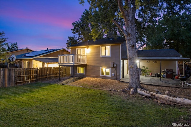 back house at dusk featuring a patio, a balcony, and a yard