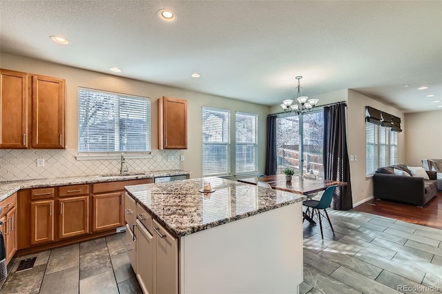 kitchen featuring pendant lighting, a notable chandelier, tasteful backsplash, a kitchen island, and a sink