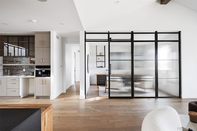 kitchen with lofted ceiling with beams, decorative backsplash, light wood-style flooring, gray cabinets, and a sink