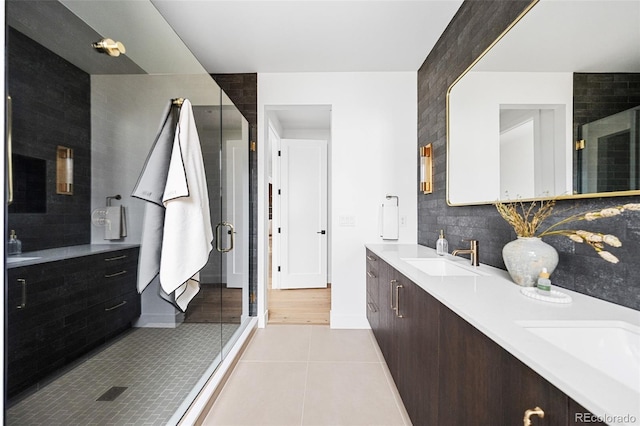 bathroom with double vanity, a stall shower, a sink, tile patterned flooring, and backsplash