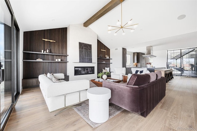 living area with beam ceiling, an inviting chandelier, light wood-style floors, a glass covered fireplace, and high vaulted ceiling