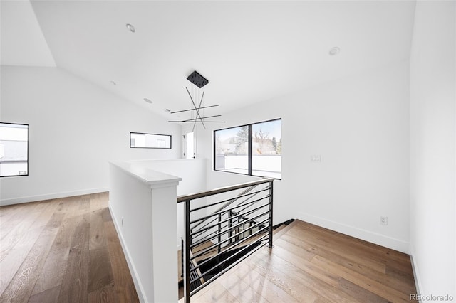 hallway featuring an upstairs landing, light wood finished floors, baseboards, and vaulted ceiling