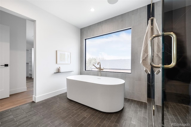 full bath featuring a shower with shower door, baseboards, a freestanding bath, and wood finished floors