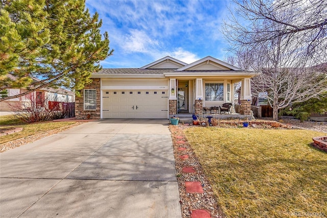 view of front of home with a porch, an attached garage, a front yard, stone siding, and driveway