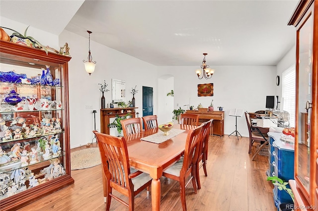 dining area featuring arched walkways, a notable chandelier, and light wood finished floors