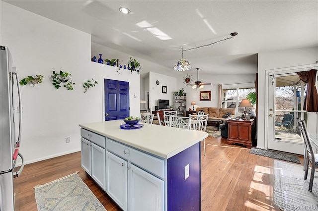 kitchen featuring a kitchen island, wood finished floors, open floor plan, light countertops, and freestanding refrigerator