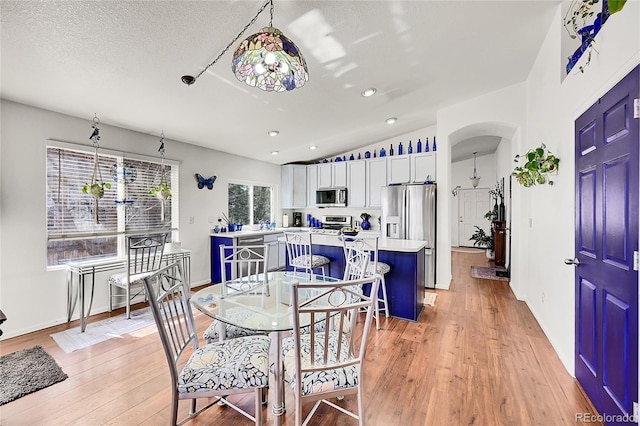 dining area with lofted ceiling, light wood-style flooring, arched walkways, and a textured ceiling