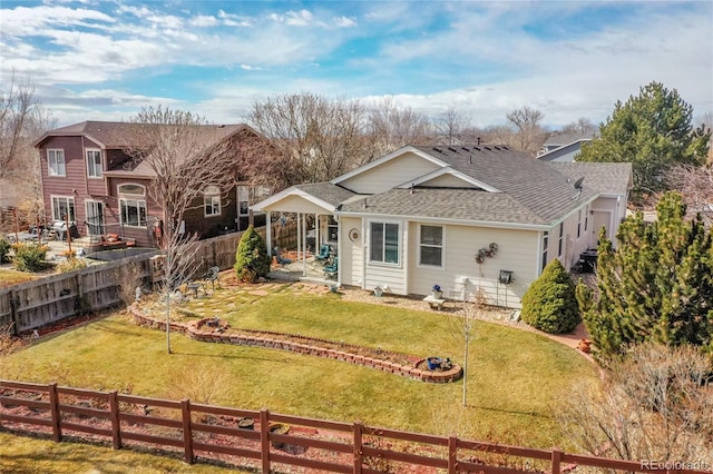 back of house with roof with shingles, a lawn, and a fenced backyard