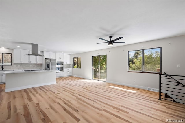 unfurnished living room with light wood finished floors, plenty of natural light, visible vents, and baseboards