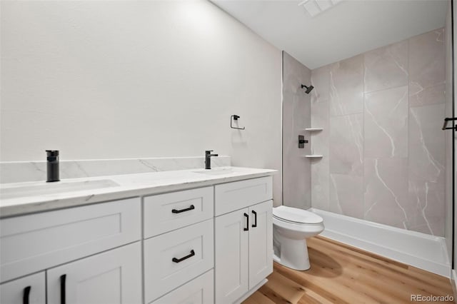 bathroom with hardwood / wood-style floors, toilet, a tile shower, and vanity